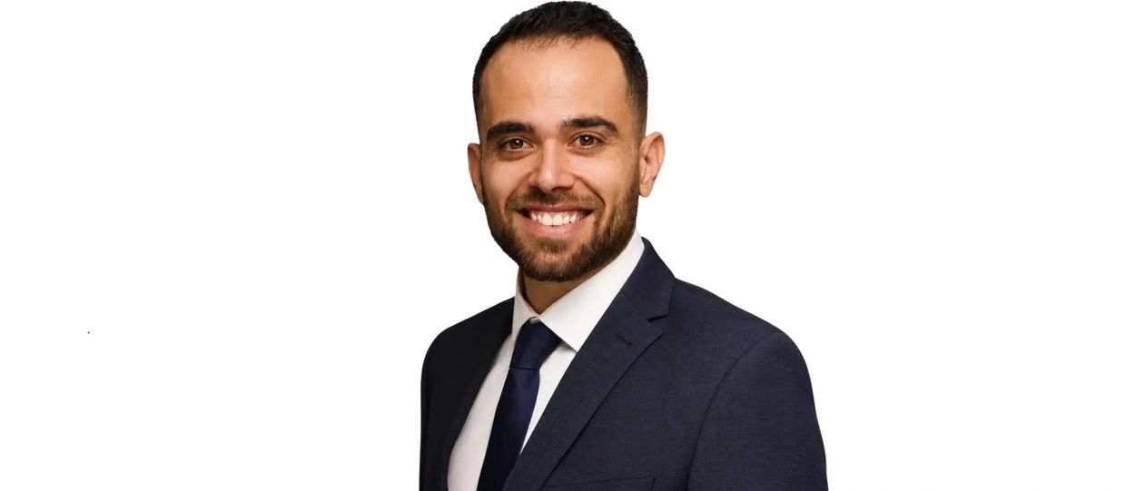 Smiling man in a dark suit and tie against a white background.