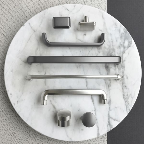 Various modern cabinet handles and knobs displayed on a round marble surface.