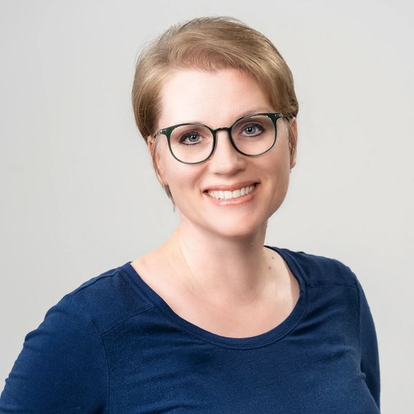 Smiling woman with glasses and short hair in a blue top.