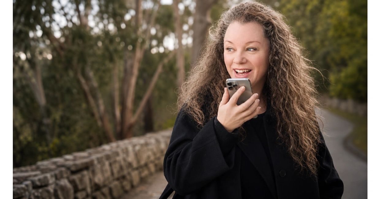 Woman with curly hair happily talking on phone outdoors.
