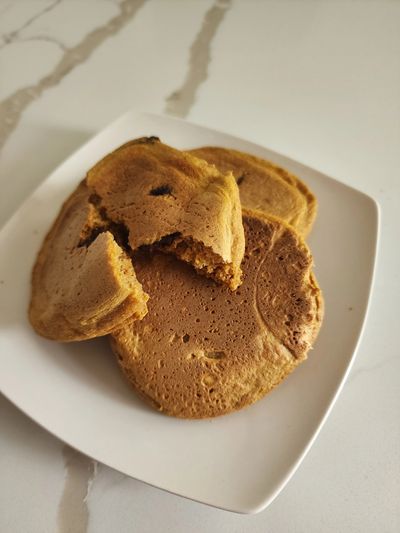 Three pancakes on a white plate, one partially eaten.