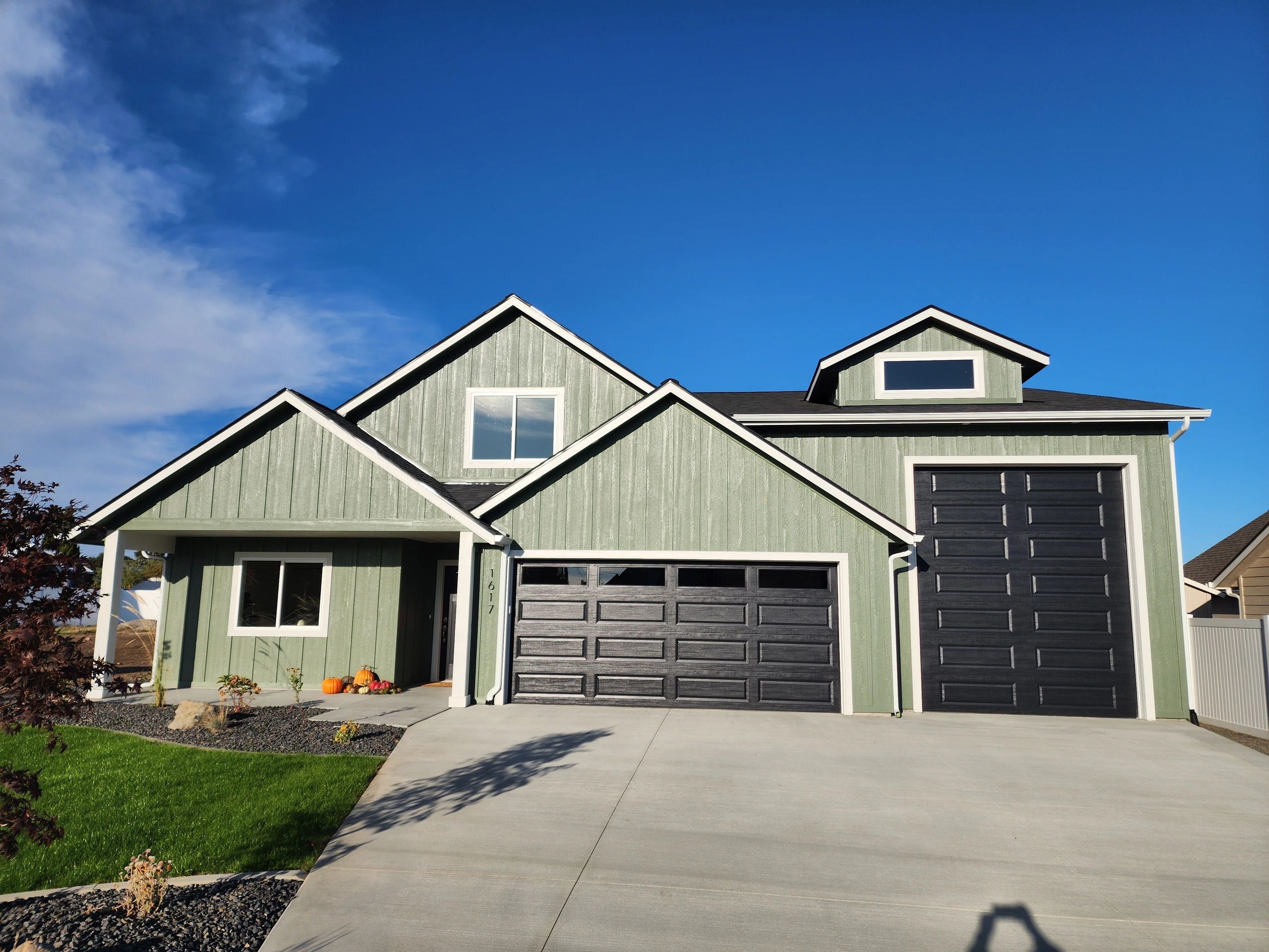 Green house with black garage doors under a clear blue sky.