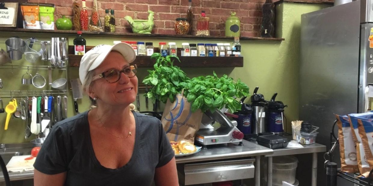 Smiling woman in a kitchen with fresh basil and cooking utensils.