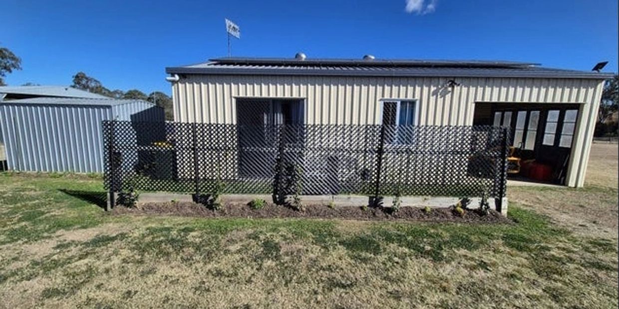 Metal shed with a small garden and lattice fence in front under a blue sky.