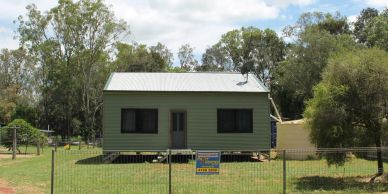 Small green house with a metal roof behind a fenced yard.