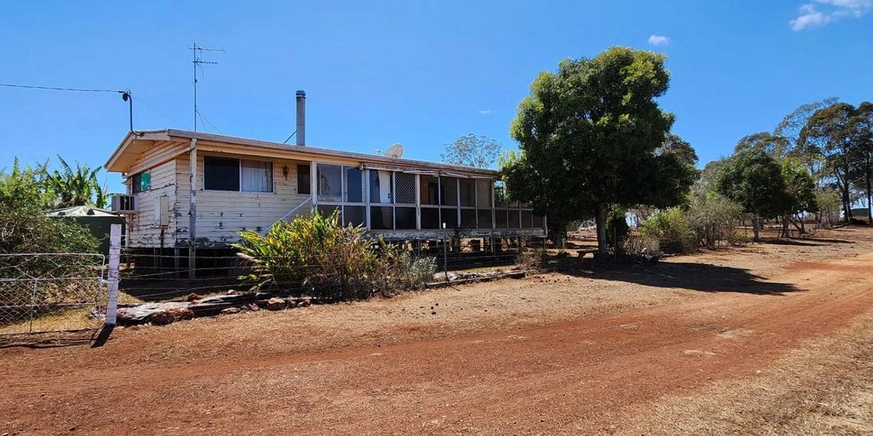 A rural house with a large porch and dry landscape under a clear blue sky.