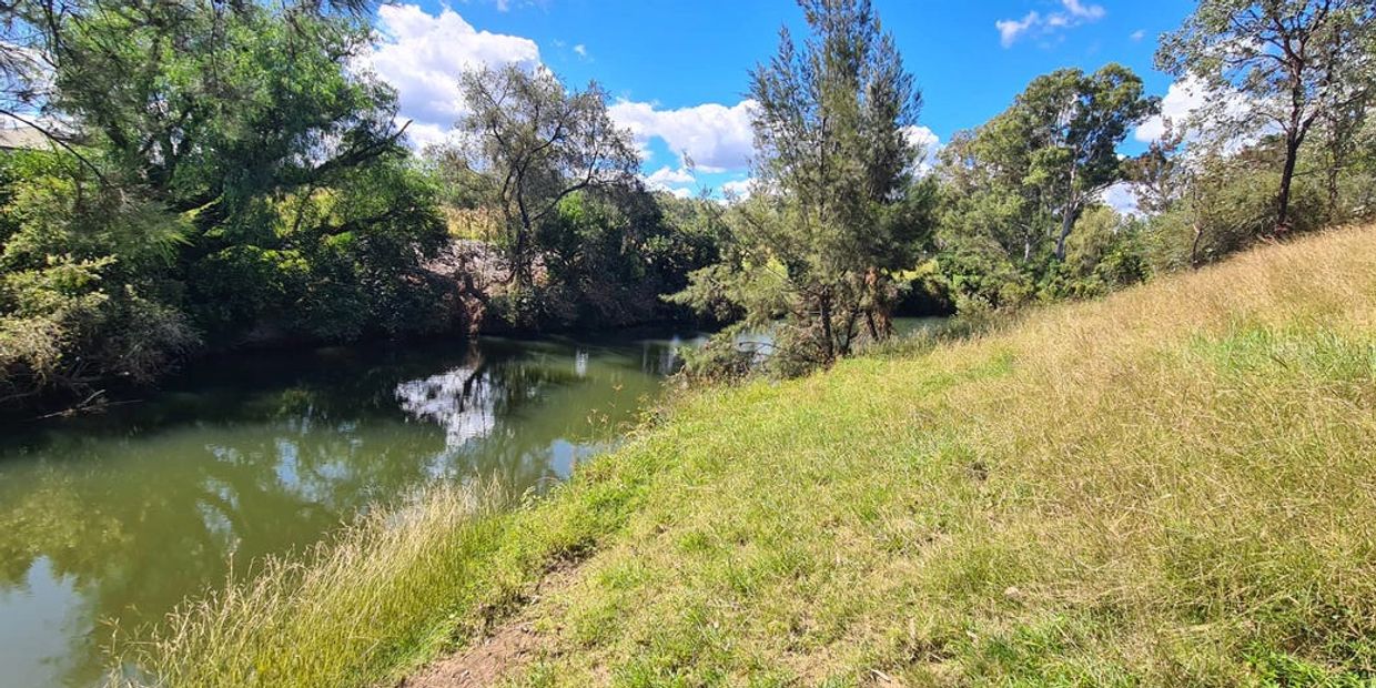 A calm river flowing beside grassy banks under a partly cloudy blue sky.