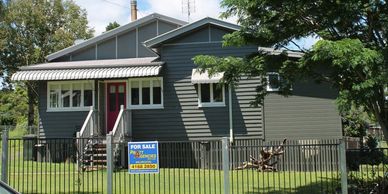 A gray house with a red door and a 'For Sale' sign in the front yard.