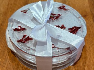 Clear resin coasters with red flower petals tied with a white ribbon on a wooden surface.