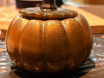 A glittery golden pumpkin-shaped container with a lid on a table.