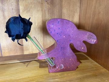 Purple bunny-shaped vase holding a single black artificial rose.