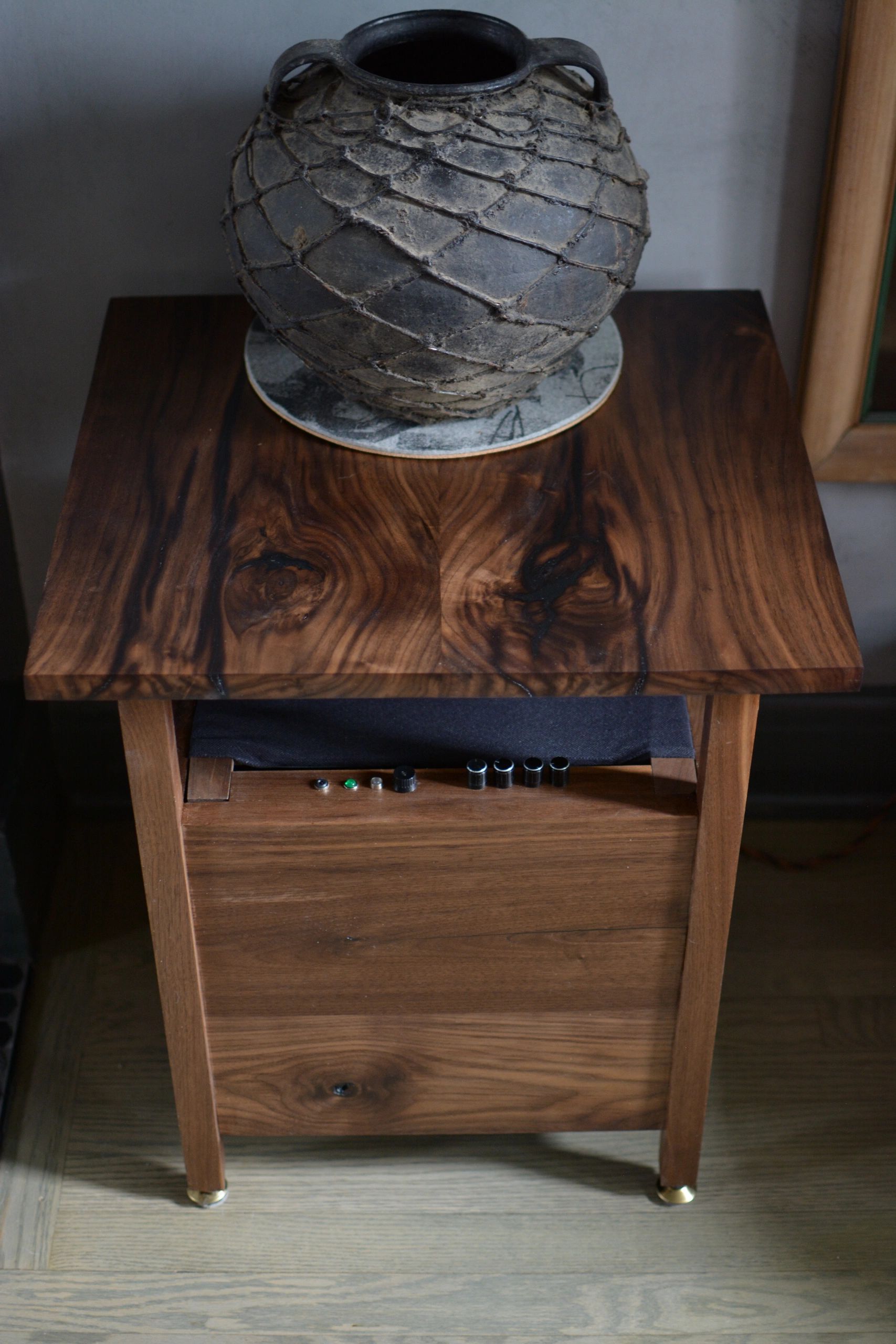 Antique clay pot with netting on a wooden stool with small items underneath.