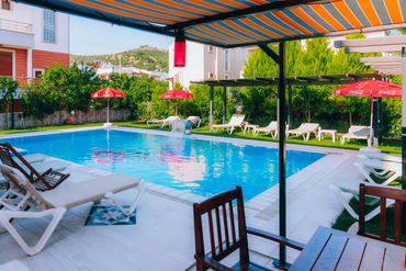 Sunny outdoor pool area with lounge chairs and striped canopy.