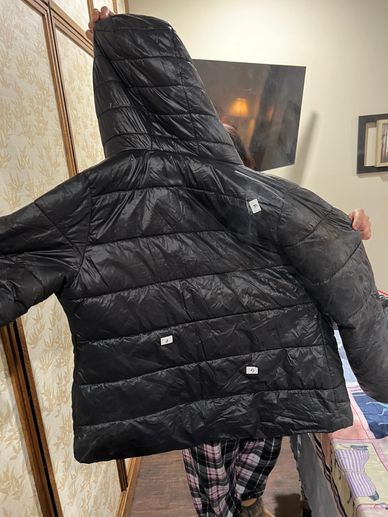 Person holding a black puffer jacket with size labels inside.