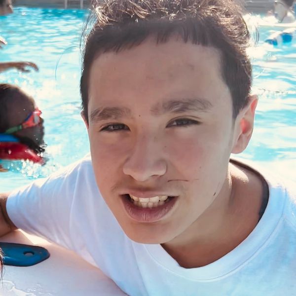 A young man smiling by the poolside on a sunny day.