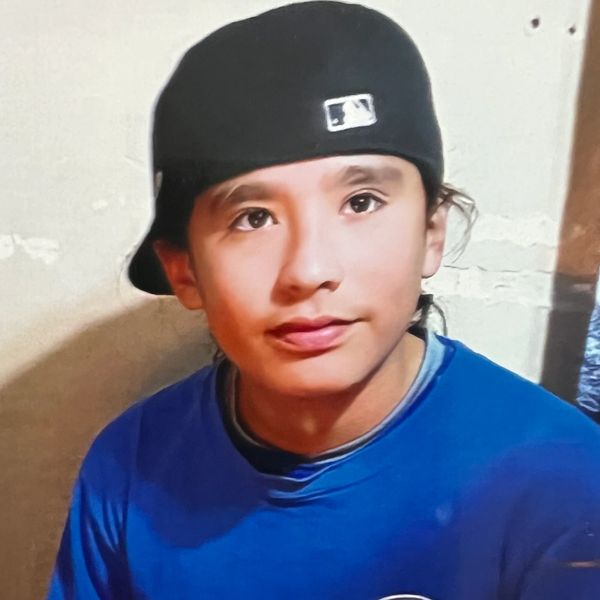 Young person in a black cap and blue shirt sitting at a table with lit candles.