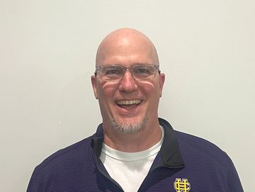 Smiling bald man wearing glasses and a dark blue shirt with a logo.