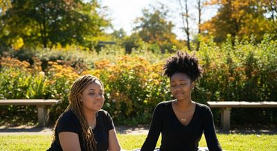 Two women sitting outdoors in a sunny park, enjoying a calm moment.