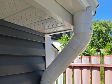 Close-up of a white rain gutter downspout on a house corner against blue sky.