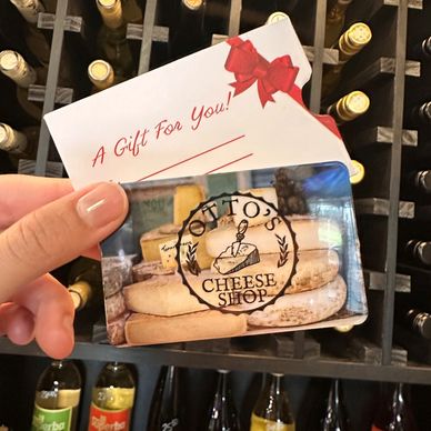 Hand holding a cheese shop gift card in front of wine bottles.