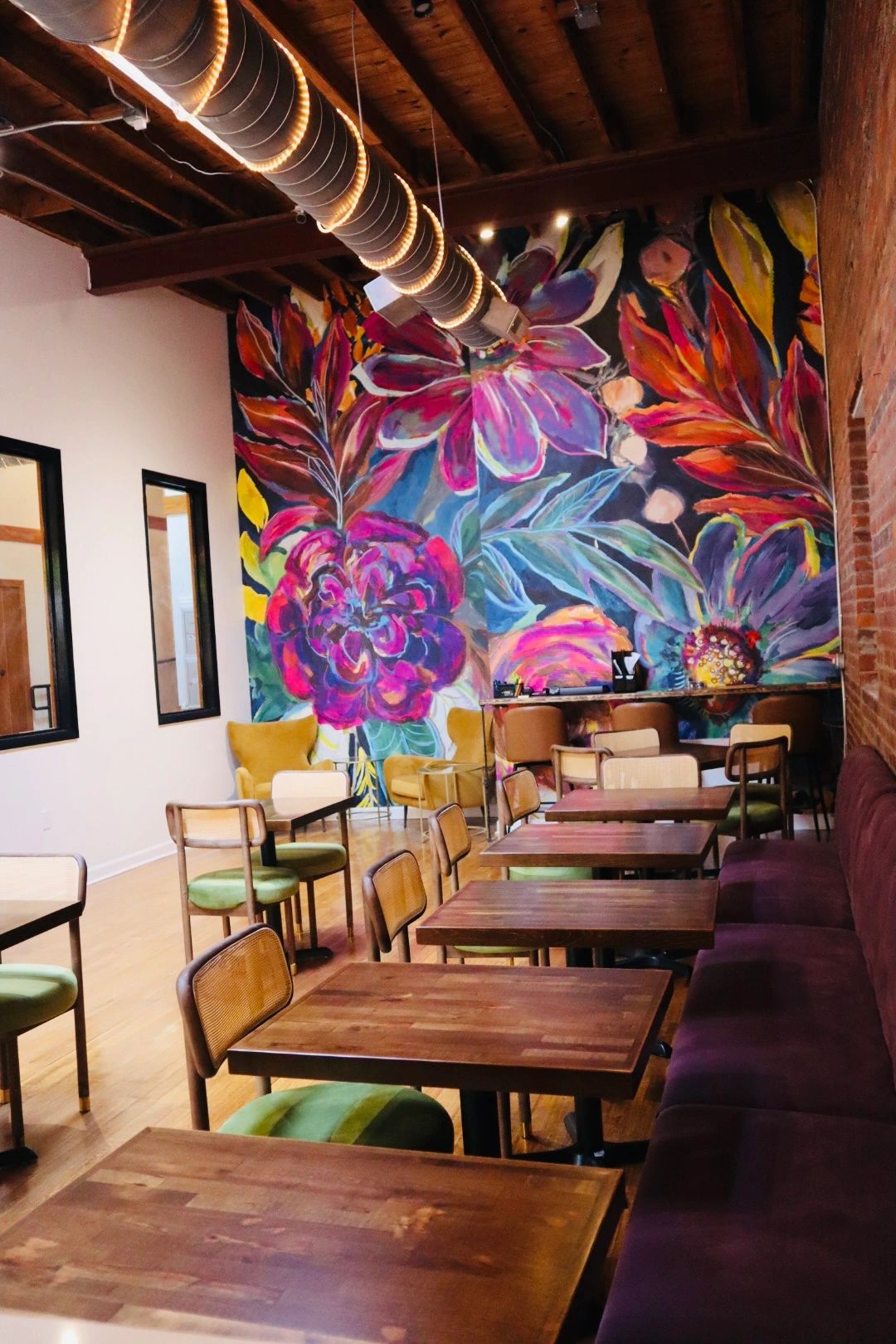 Cozy cafe interior with wooden tables, colorful chairs, and a vibrant floral mural.