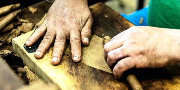 Hands rolling a cigar by hand on a wooden surface.