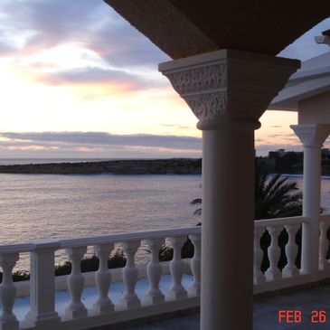 Sunset view over the ocean from a balcony with ornate white columns.