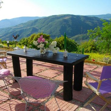Outdoor patio with purple chairs and a black table overlooking green hills.