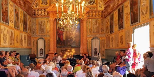 Audience watching a musical performance in an ornate hall with chandeliers.