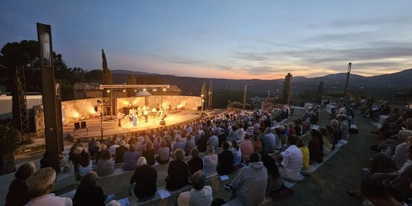 Outdoor amphitheater concert at sunset with a large audience.