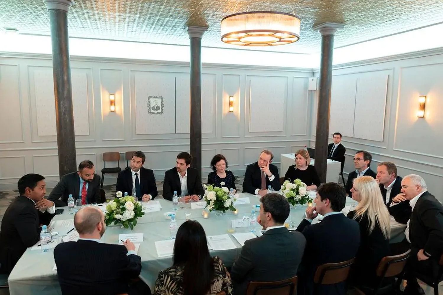 A formal business meeting with professionals seated around a large table in a well-lit room.
