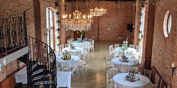 Elegant event space with round tables, chandeliers, and a spiral staircase.