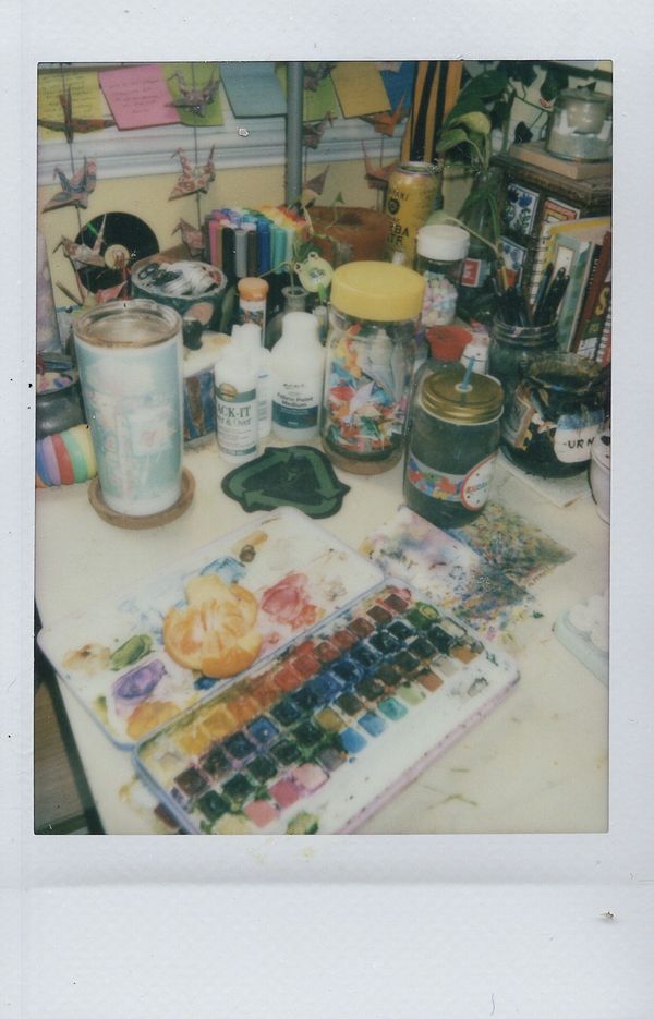 A colorful artist's workspace with paints, markers, and origami cranes.