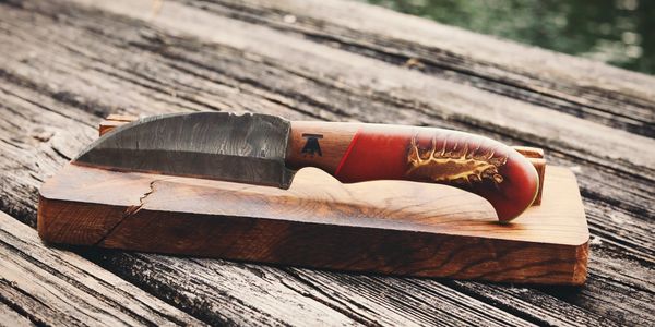 A handcrafted knife with a wooden handle on a wooden block outdoors.