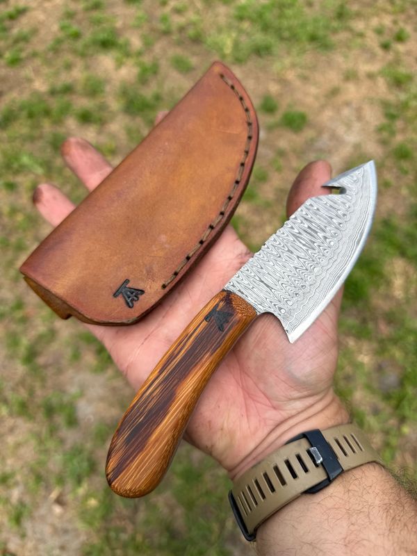 Hand holding a knife with a wooden handle and a leather sheath.