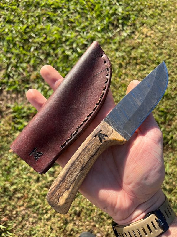 Hand holding a handcrafted knife with a wooden handle and leather sheath.