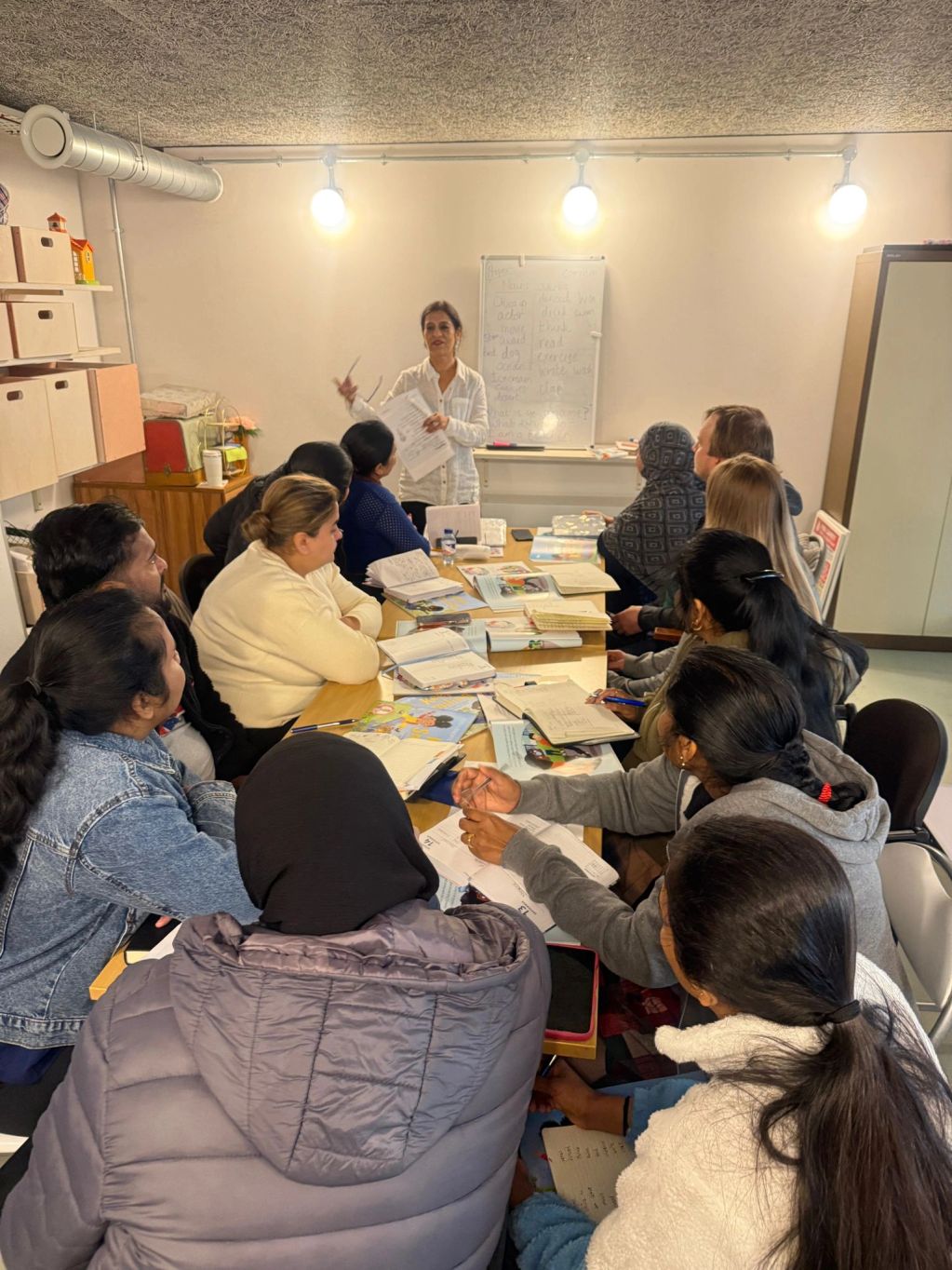 A group learning session with a teacher and engaged students around a table.