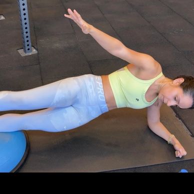 Woman performing a side plank exercise on a mat with a Bosu ball.