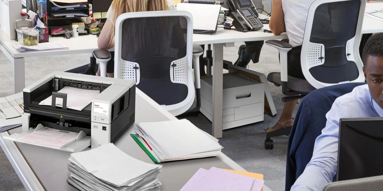 Busy modern office with employees working and a scanner on the desk.