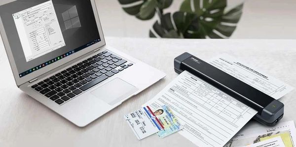 A laptop and portable scanner with documents on a white table.