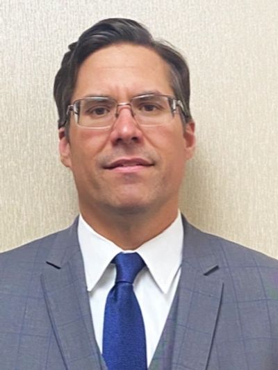 Man in gray suit and blue tie with glasses.