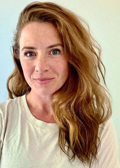 Woman with long red hair and freckles smiling.