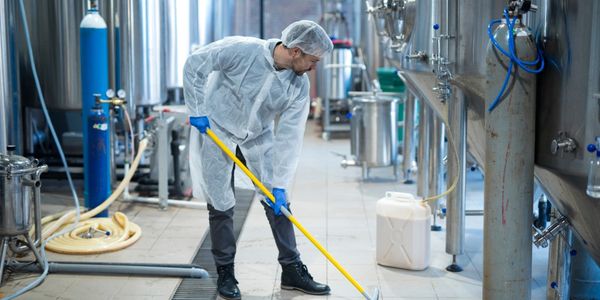 Professional industrial cleaner in protective uniform cleaning floor of food processing plant.