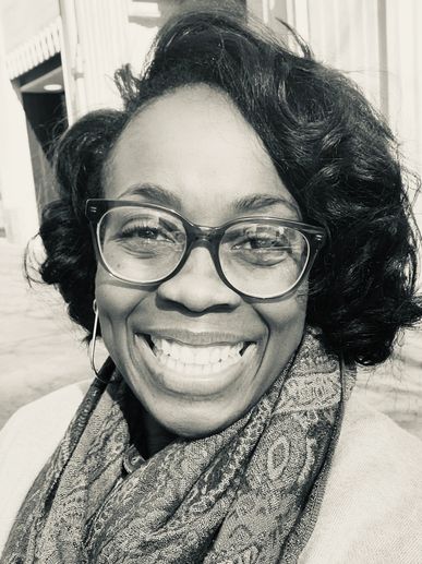 A smiling woman with glasses and a patterned scarf.
