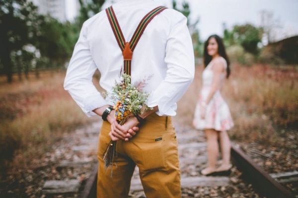 man surprising his beautiful fiance with a  bouquet of wildflowers on old railroad