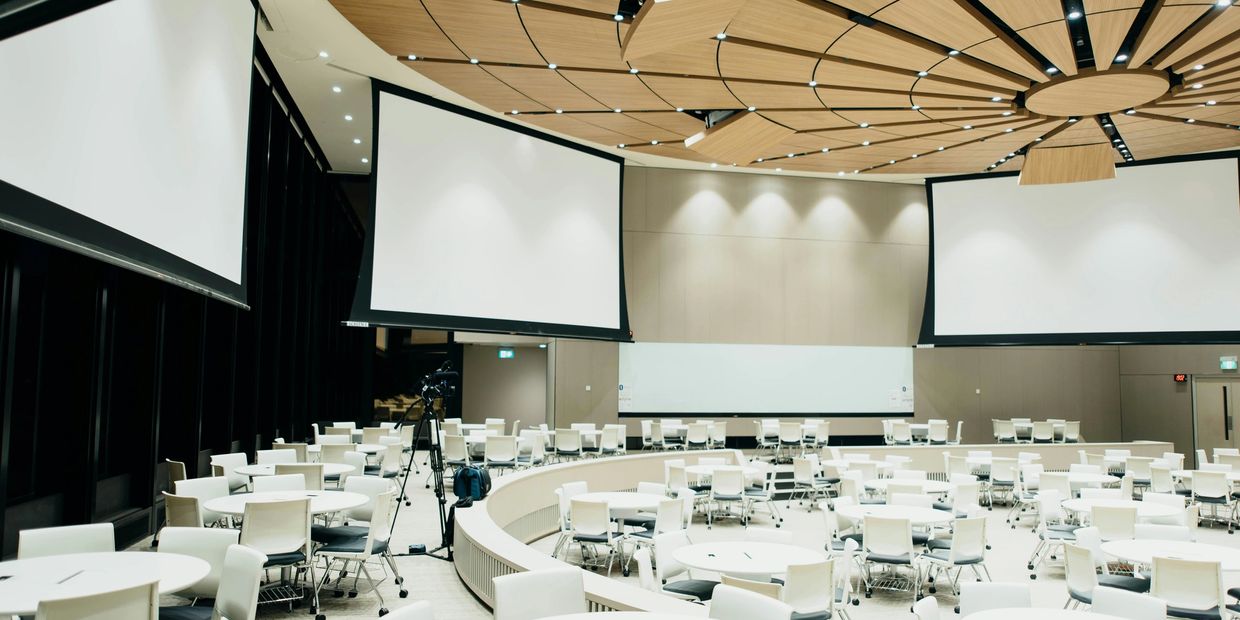 A modern conference room with round tables and multiple projection screens.