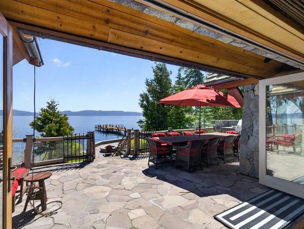 Outdoor patio with dining area, red umbrella, and lake view with dock.