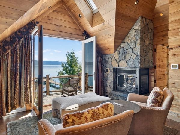Cozy wooden cabin living room with stone fireplace and lake view.