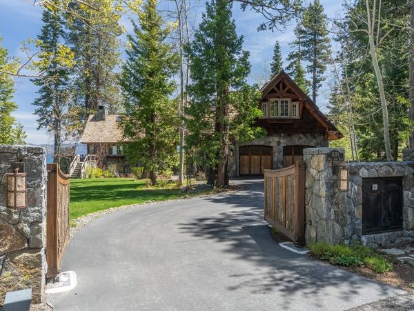 A scenic driveway leads to a rustic stone and wood house surrounded by tall trees.