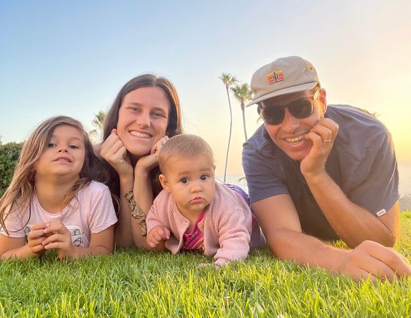 A happy family of four lying on grass during sunset.